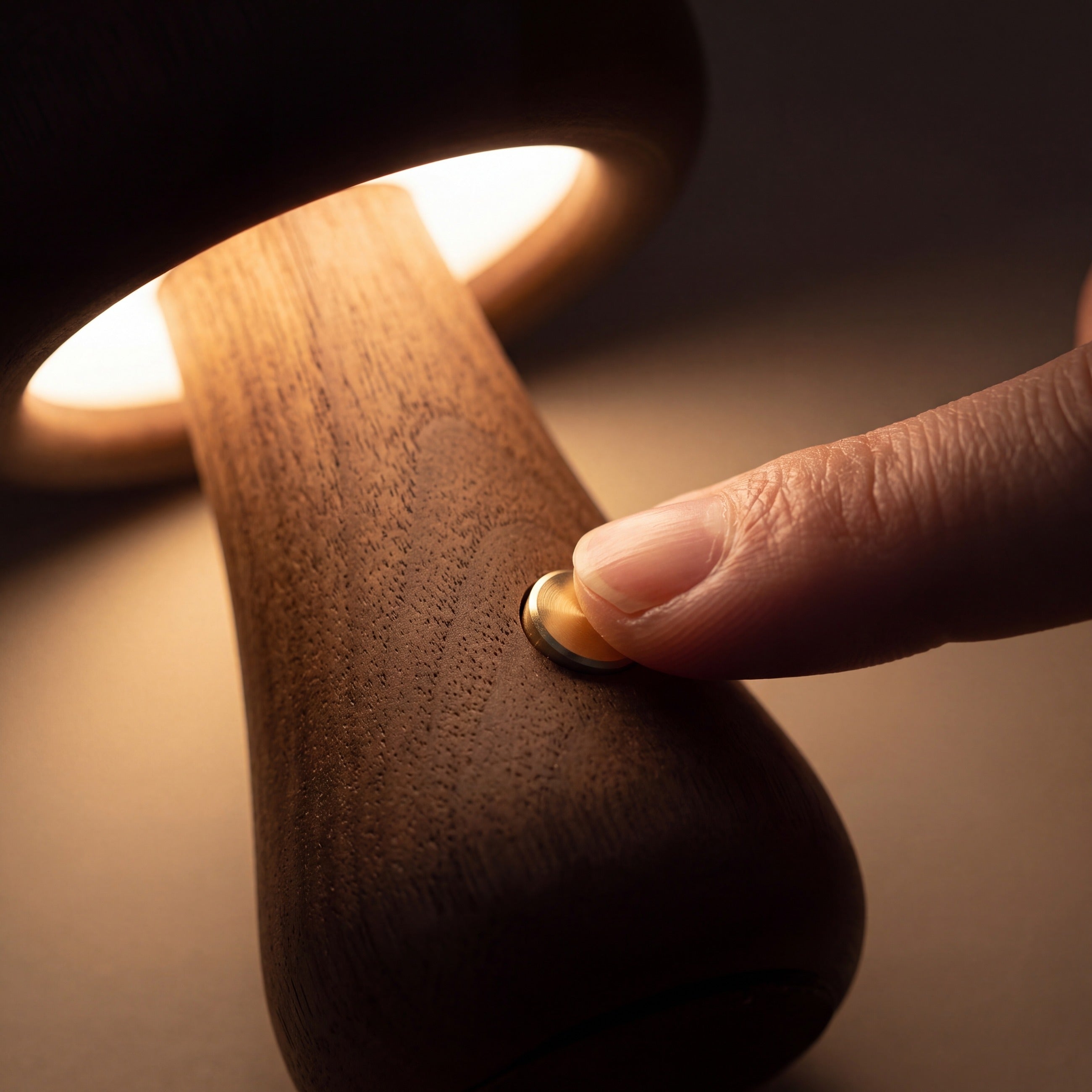 A fingertip on the brass button set into the walnut stem — touch to dim