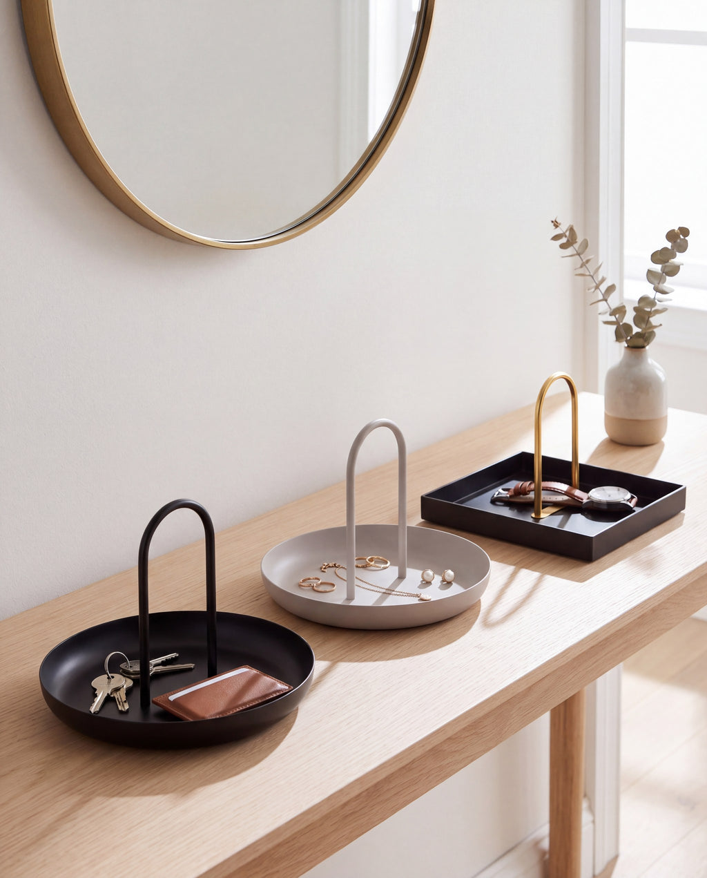 The Zivol Arc Trio: black round, warm grey round and black square with brass arch on one console