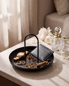 Zivol Arc black round tray filled with gold jewellery, keys and a wallet beside a crystal perfume bottle