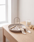 Zivol Arc warm grey tray with jewellery and a silk ribbon on a pale oak dressing table