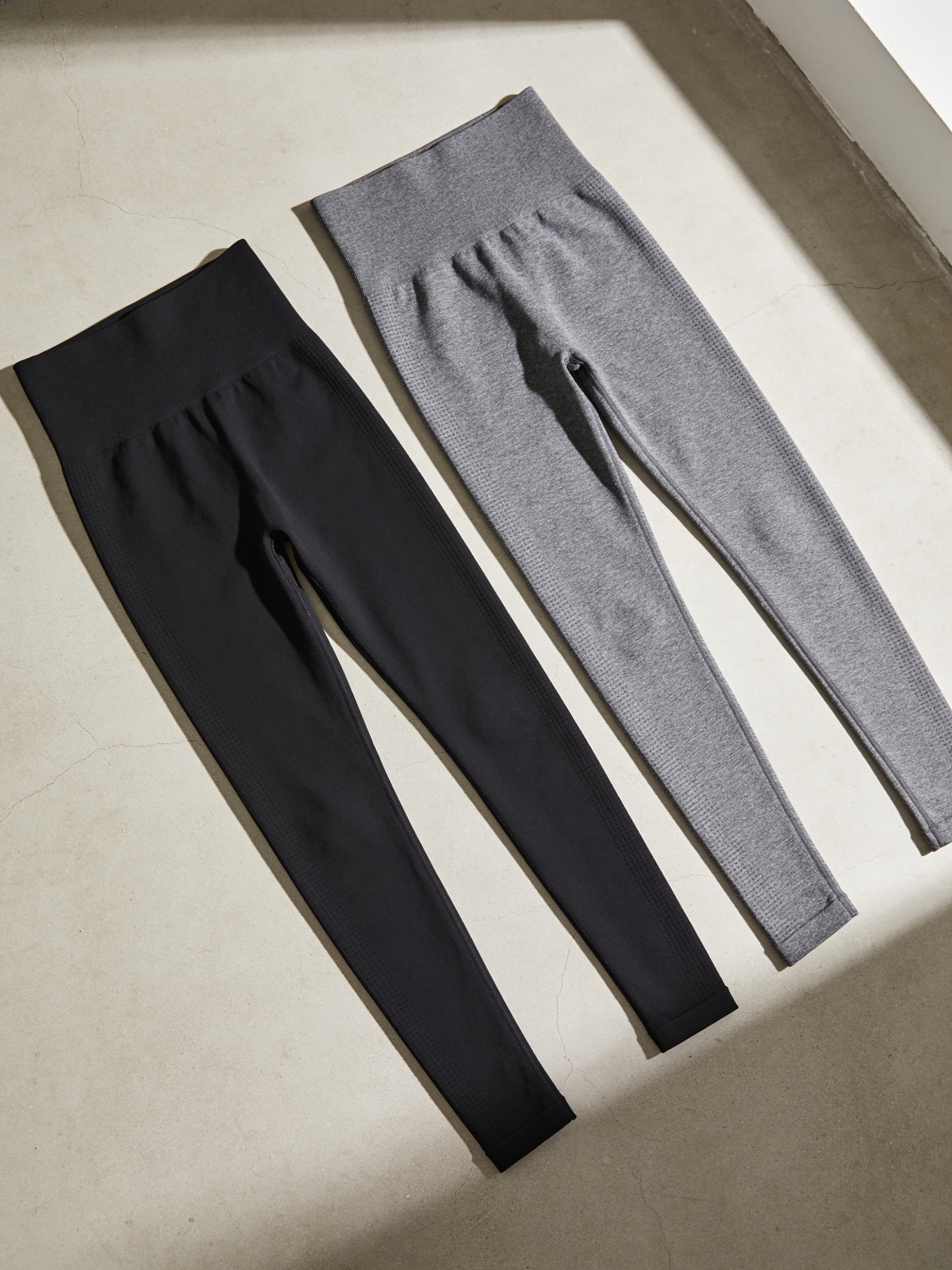 Black and grey Zivol Claim leggings laid flat side by side, both with the handprint print